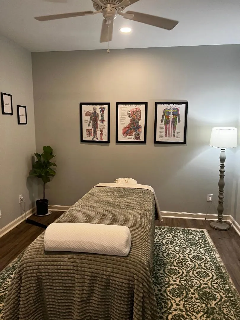 A Green Owl treatment room: massage table with a green blanket, anatomy prints on the wall and a floor lamp